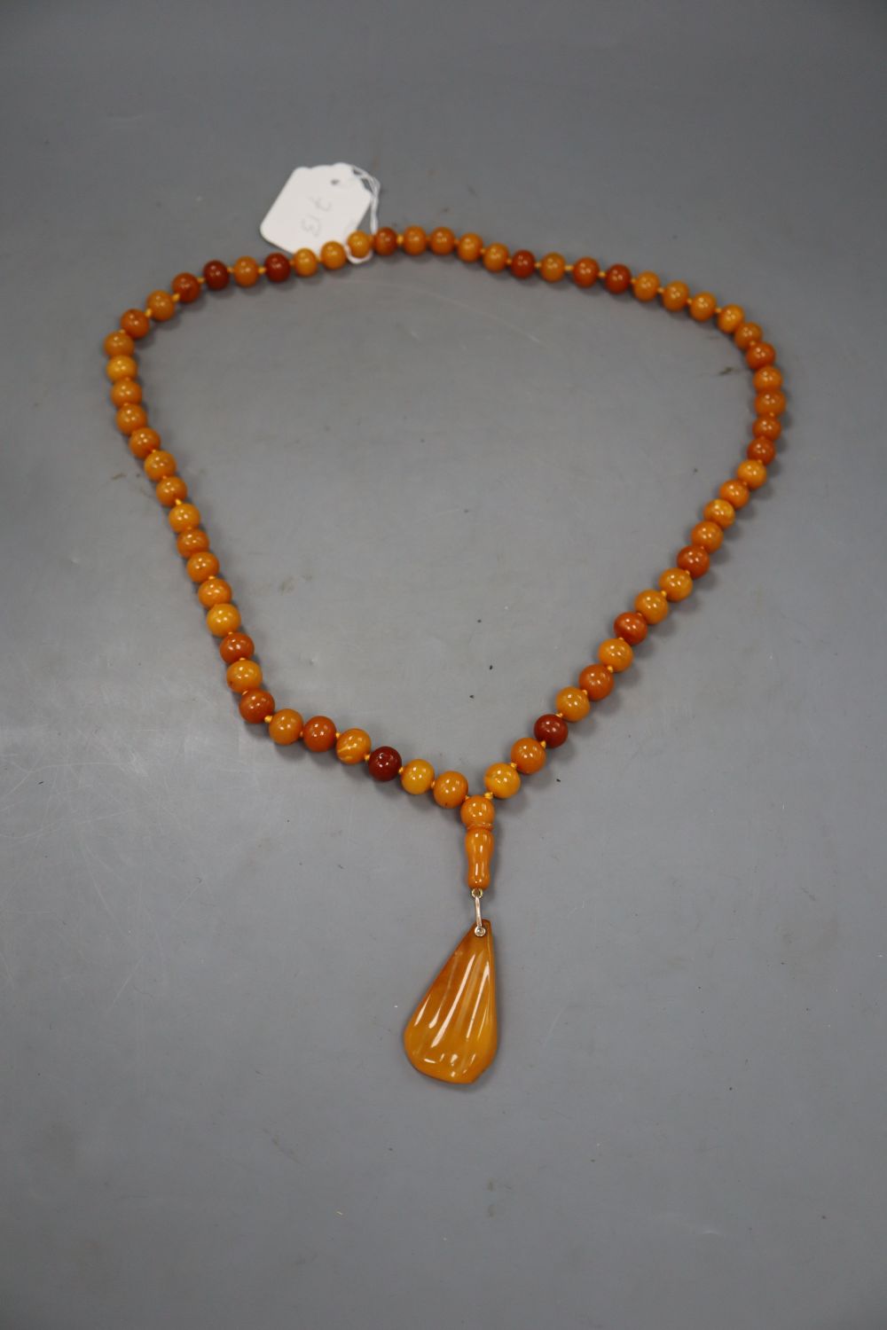 A single strand circular amber bead necklace, with pear shaped amber pendant, gross 74 grams.
